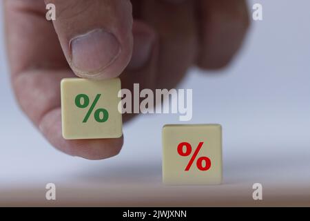 Hand hält ein Stück Scrabble mit einem grünen Prozentzeichen, das symbolisiert, dass die Zinssätze von negativ auf positiv abgehen. Stockfoto