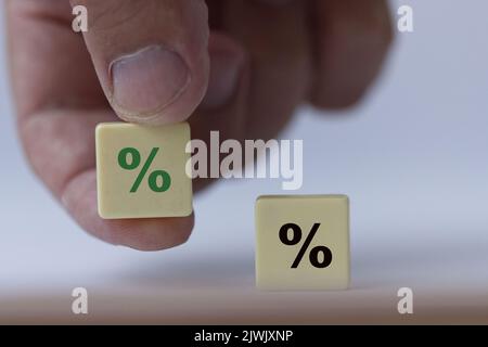 Hand hält ein Stück Scrabble mit einem grünen Prozentzeichen, das symbolisiert, dass die Zinsen steigen. Stockfoto