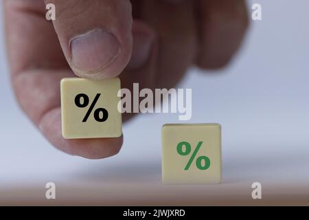 Hand hält ein Stück Scrabble mit schwarzem Prozentzeichen, das symbolisiert, dass die Zinssätze von positiv zu neutral werden. Stockfoto