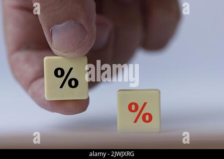 Hand hält ein Stück Scrabble mit schwarzem Prozentzeichen, das symbolisiert, dass die Zinssätze von negativ auf neutral abfallen. Stockfoto