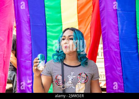 Goiânia, Goias, Brasilien – 04. September 2022: Ein lächelndes Mädchen, ihr Haar blau gefärbt mit Regenbogenfahnen im Hintergrund. Foto während der Parade. Stockfoto