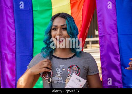 Goiânia, Goias, Brasilien – 04. September 2022: Ein lächelndes Mädchen, ihr Haar blau gefärbt mit Regenbogenfahnen im Hintergrund. Foto während der Parade. Stockfoto