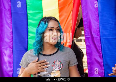 Goiânia, Goias, Brasilien – 04. September 2022: Ein lächelndes Mädchen, ihr Haar blau gefärbt mit Regenbogenfahnen im Hintergrund. Foto während der Parade. Stockfoto