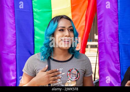 Goiânia, Goias, Brasilien – 04. September 2022: Ein lächelndes Mädchen, ihr Haar blau gefärbt mit Regenbogenfahnen im Hintergrund. Foto während der Parade. Stockfoto