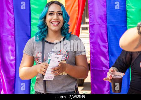 Goiânia, Goias, Brasilien – 04. September 2022: Ein lächelndes Mädchen, ihr Haar blau gefärbt mit Regenbogenfahnen im Hintergrund. Foto während der Parade. Stockfoto