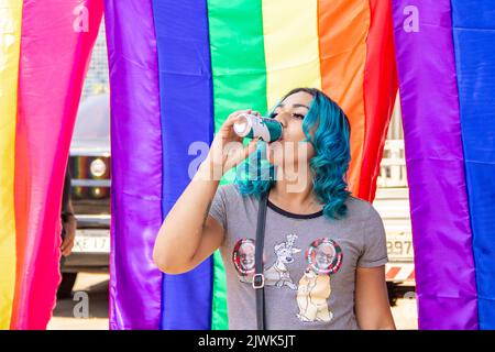 Goiânia, Goias, Brasilien – 04. September 2022: Ein lächelndes Mädchen, ihr Haar blau gefärbt mit Regenbogenfahnen im Hintergrund. Foto während der Parade. Stockfoto