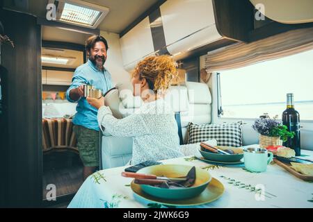 Alternatives Lifestyle-Konzept. Glückliches Paar, das mit dem Wohnmobil unterwegs ist und drinnen am Tisch sitzt Stockfoto