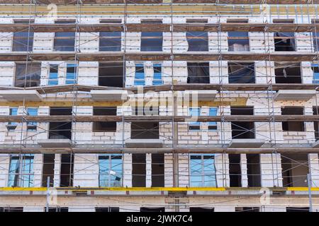 Isolierung der Außenwände eines Gebäudes im Bau. Die Wände des im Bau befindlichen Gebäudes sind von Gerüsten für Arbeiten umgeben Stockfoto