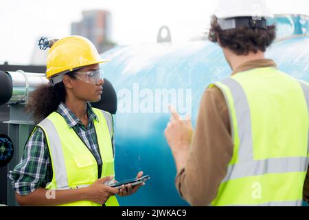 Junge Frau und Mann Ingenieur Untersuchung Pipeline und suchen digitale Tablette in der Fabrik, Mechaniker oder Techniker Inspektor Klempner Ventil und sprechen Stockfoto