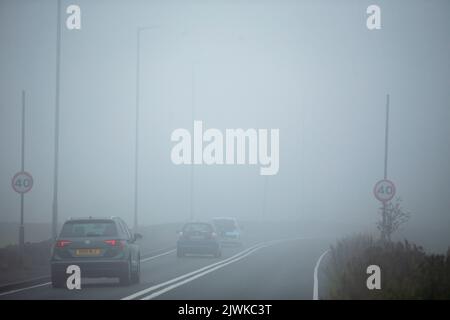 Auto-, Transporter- und LKW-Fahrer mit Scheinwerfern fahren an einem 40 mph-Warnschild auf der Brighouse und Denholmgate Road, West Yorkshire, Großbritannien, vorbei, in sehr dichtem Nebel. Stockfoto