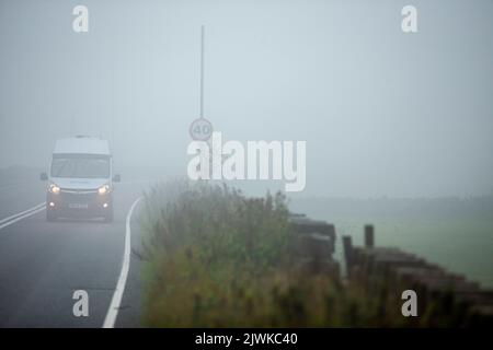 Auto-, Transporter- und LKW-Fahrer mit Scheinwerfern fahren an einem 40 mph-Warnschild auf der Brighouse und Denholmgate Road, West Yorkshire, Großbritannien, vorbei, in sehr dichtem Nebel. Stockfoto