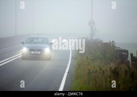 Auto-, Transporter- und LKW-Fahrer mit Scheinwerfern fahren an einem 40 mph-Warnschild auf der Brighouse und Denholmgate Road, West Yorkshire, Großbritannien, vorbei, in sehr dichtem Nebel. Stockfoto