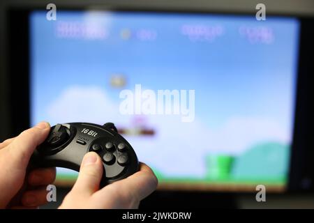 Spielt ein Retro-Spiel auf dem Fernseher, während der klassische schwarze Joystick gedrückt wird Stockfoto