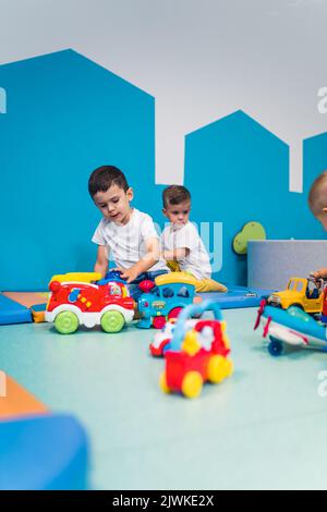 Spielzeit im Kindergarten. Kleinkinder kaukasische Jungen sitzen auf dem Boden und spielen mit bunten Plastikautos, Booten, Flugzeugen und anderen Spielzeugen. Hochwertige Fotos Stockfoto