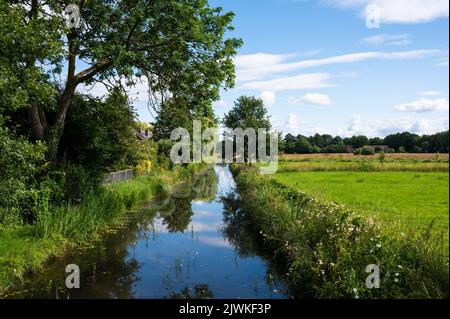 Creek rund um das Dorf Zwolle, Gelderland, Niederlande mit grünen Bäumen, die sich gegen den blauen Himmel spiegeln Stockfoto