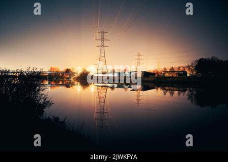 Newburn UK: 6.. märz 2022: Newburn Riverside bei Nacht elektrische Pylons, Ruderclub und noch Fluss mit warm glühendem Industrielicht Stockfoto