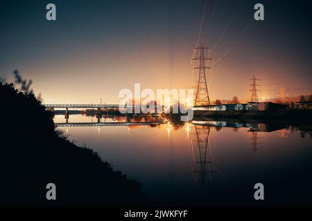 Newburn UK: 6.. märz 2022: Newburn Riverside bei Nacht elektrische Pylons, Ruderclub und noch Fluss mit warm glühendem Industrielicht Stockfoto