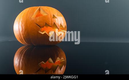 Nahaufnahme von geschnitztem gruseligen halloween Kürbis vor grauem Hintergrund Stockfoto