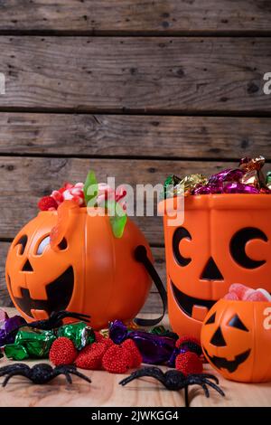 Nahaufnahme eines Kürbis-förmigen Eimers voller halloween-Süßigkeiten und Spielzeug auf einer Holzoberfläche Stockfoto