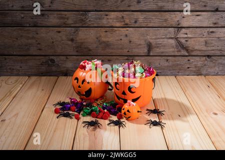 Kürbis geformter Eimer voller halloween Süßigkeiten und Spielzeug auf Holzfläche Stockfoto