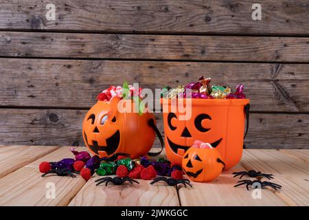 Kürbis geformter Eimer voller halloween Süßigkeiten und Spielzeug auf Holzfläche Stockfoto