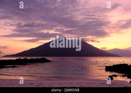 Indonesia Alor Island - Felsenstrand und Vulkan bei Sonnenuntergang Stockfoto