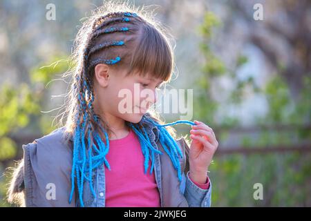 Profilportrait eines ziemlich lächelnden jungen Teenagers in legerer Kleidung und blauen Bändern, die im Sommer oder Frühling in langen Zöpfen im Freien geflochten sind Stockfoto