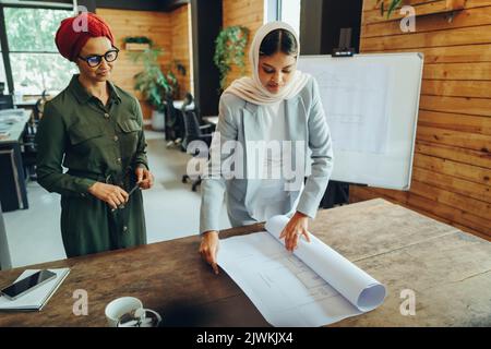 Zwei muslimische Architekten arbeiten in einem modernen Büro mit Blaupause-Zeichnungen. Zwei kreative Geschäftsfrauen planen ein innovatives Projekt. Designerinnen Stockfoto