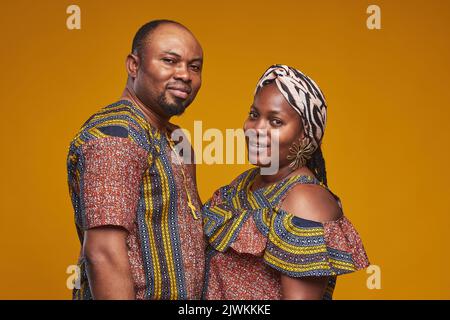 Porträt eines afrikanischen Paares in Nationalkostümen, das vor der Kamera vor gelbem Hintergrund lächelt Stockfoto