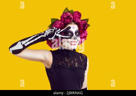 Glückliche Frau, die für den Tag der Toten oder Halloween mit einem Lächeln und einer Friedensgeste gekleidet ist Stockfoto