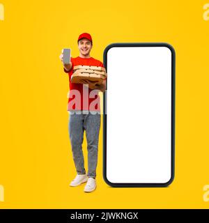 Lieferung Guy Holding Pizzakisten Stehen In Der Nähe Von Handy, Gelber Hintergrund Stockfoto