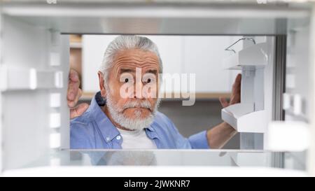 Hungriger Älterer Mann, Der Zu Hause Leere Regale Im Kühlschrank Ansieht Stockfoto