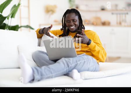 Lächelnder junger schwarzer Mann, der zu Hause mit dem Laptop Videoanruf macht Stockfoto