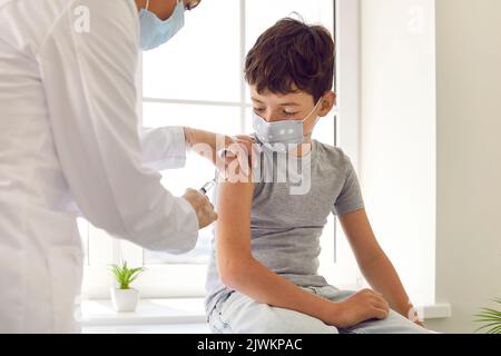 Krankenschwester, die dem Schulkind Injektion gibt, um ihn vor Grippe, Kovid oder Monkeypox-Infektion zu schützen Stockfoto