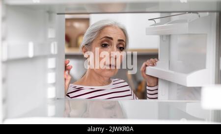 Traurige Ältere Frau, Die Zu Hause Leere Regale Im Kühlschrank Ansieht Stockfoto