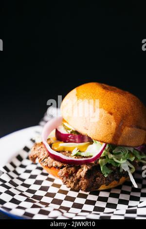 Doble Cheeseburger mit Gemüse auf einem weißen Teller auf einem schwarzen Hintergrund Stockfoto