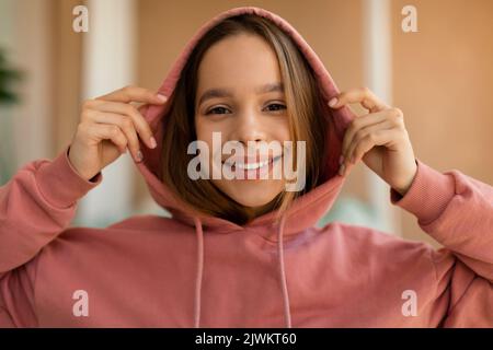 Happy stylish Teenager-Mädchen trägt Kapuze und lächelt an der Kamera, ruht sich zu Hause und posiert Stockfoto