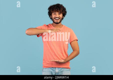 Fröhlicher, hübscher inder, der etwas Unsichtbares in seinen Händen zeigt Stockfoto