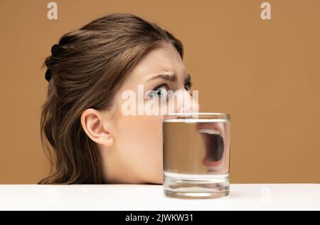 Schrei. Moderne Kunstfotografie. Das Gesicht des schönen Mädchens durch ein Glas Wasser. Objektverzerrung, optische Täuschung. Minimalistische zeitgenössische Kunst Stockfoto