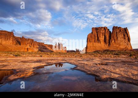 Die drei Gerüchte spiegelten sich in einem kurzlebigen Regenwasserbecken im Arches National Park, Moab, Utah, wider. Abschnitt „Courthouse Towers“. Stockfoto