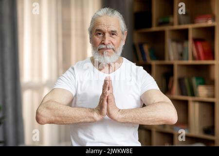 Porträt eines älteren Mannes in weißem T-Shirt, der zu Hause meditiert Stockfoto