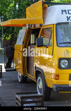 Gelber Minibus im Stadtpark, der als Verkaufsstand für Kaffee genutzt wird. Fun Fahrzeug für Snack Lieferung Verkauf Reise. Roadtrip auf gelb V Stockfoto