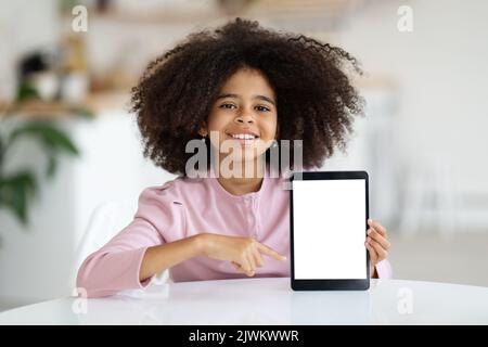 Nettes schwarzes Mädchen Schuler zeigt digitale Tablette, mockup Stockfoto