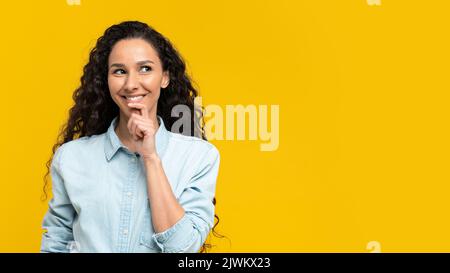 Fröhliche nachdenkliche junge Frau im lässigen Outfit, die auf leeren Raum über gelbem Studiohintergrund, Bannerdesign schaut Stockfoto