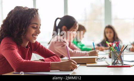 Schwarz Schulmädchen Schreiben Lernen Mit Multikulturellen Klassenkameraden Im Klassenzimmer, Panorama Stockfoto