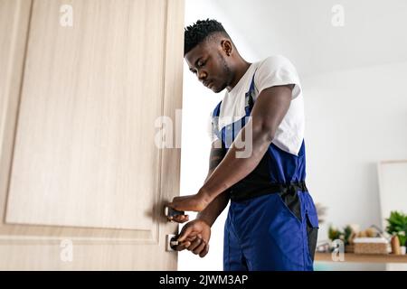 Schwarzer Handyman Trägt Overall, Einheitliche Befestigungstür, Die Schloss Im Innen- Oder Außenbereich Installiert Stockfoto