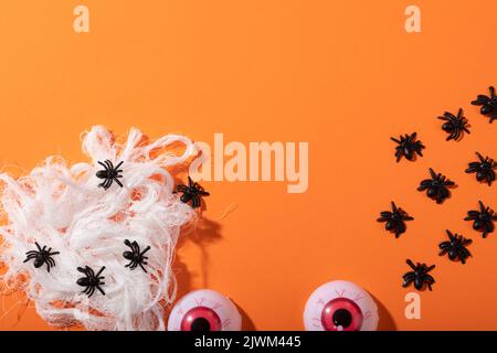 Mehrere Spider-Spielzeug bilden ein Spinnennetz und gruselige Augen Spielzeug mit Kopieplatz auf orangefarbenem Hintergrund Stockfoto