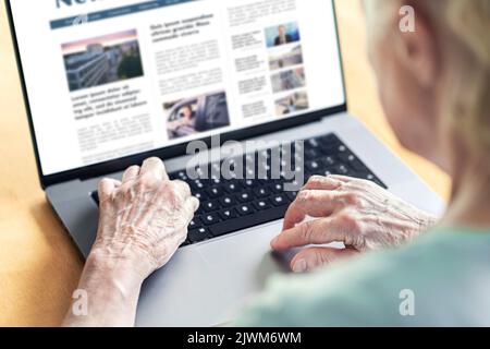 Nachrichten-Website in Laptop einer alten Frau. Älterer und Oma lesen digitale Zeitung mit Computer. Online-Magazin oder Webartikel auf dem Bildschirm. Stockfoto