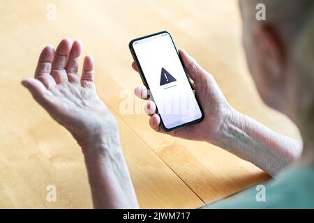 Leitender Mitarbeiter, der Probleme mit Telefon und Technologie hat. Alte Frau mit Fehlermeldung auf dem Smartphone-Bildschirm. Frustrierte Dame mit technischen Problemen. Stockfoto