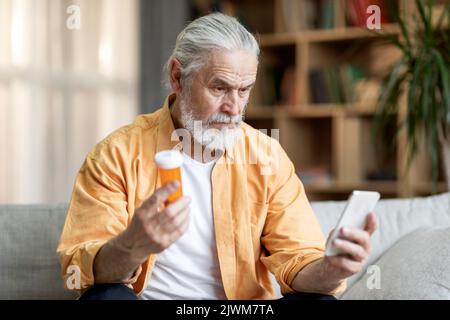 Konzentrierter älterer Mann, der Medizin und Smartphone hält Stockfoto